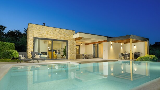Una casa moderna con piscina, puertas de vidrio amplias y mobiliario exterior.