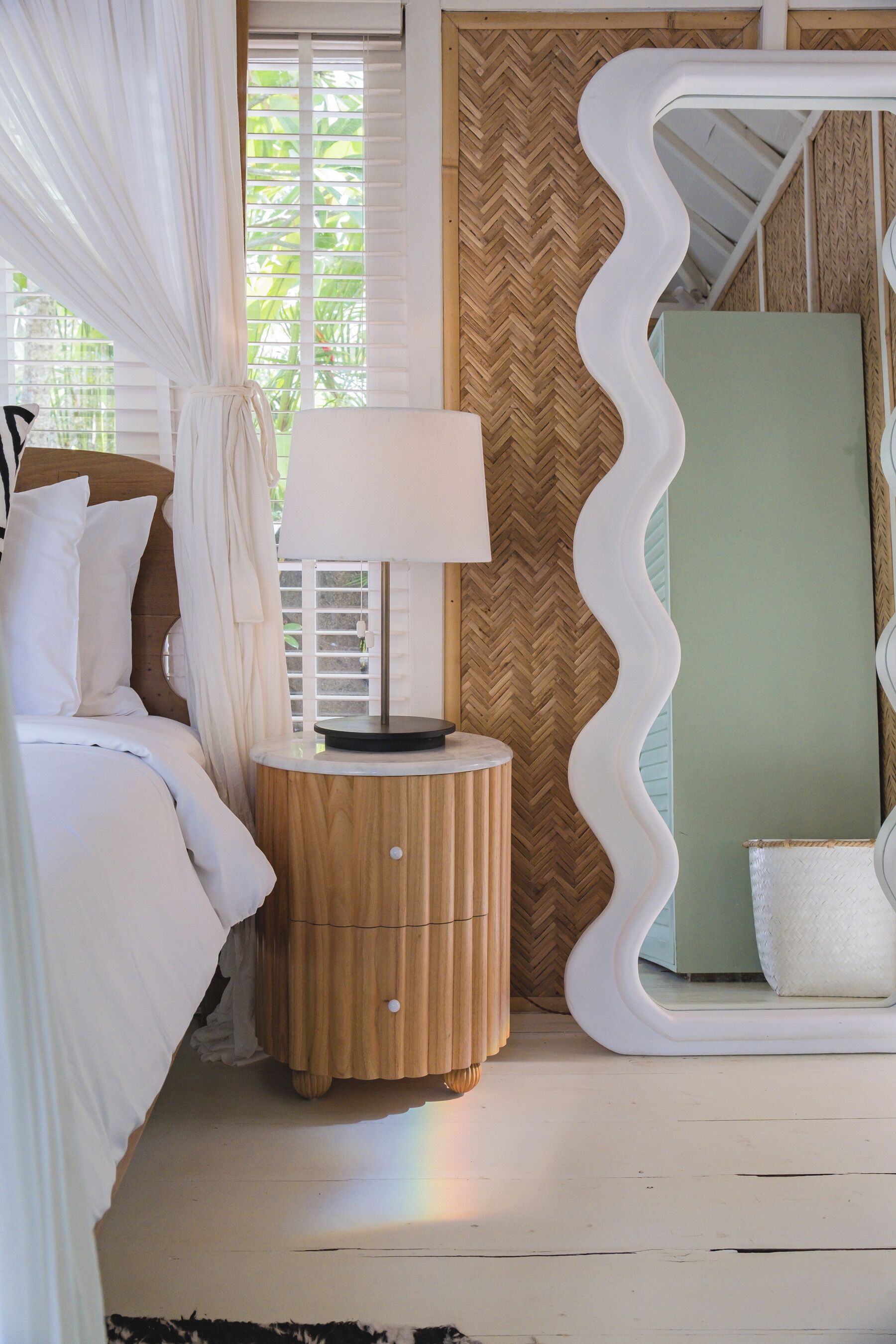 Een slaapkamer met een bed, nachtkastje met lamp, spiegel en een wand met een herringbone-patroon.