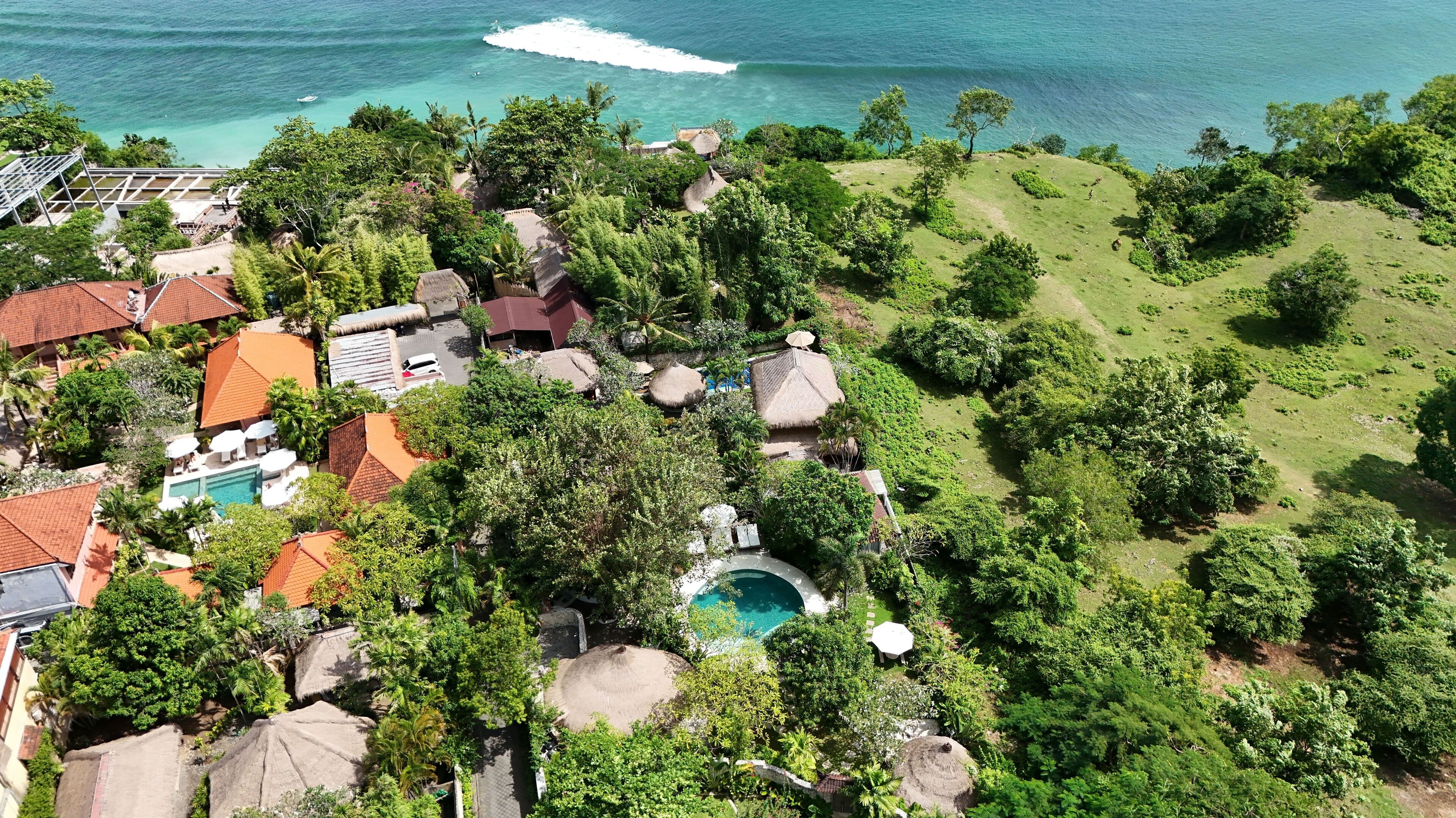 An aerial view of a resort with a swimming pool, thatched-roof structures, and lush greenery.