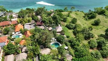 An aerial view of a resort with a swimming pool, thatched-roof structures, and lush greenery.