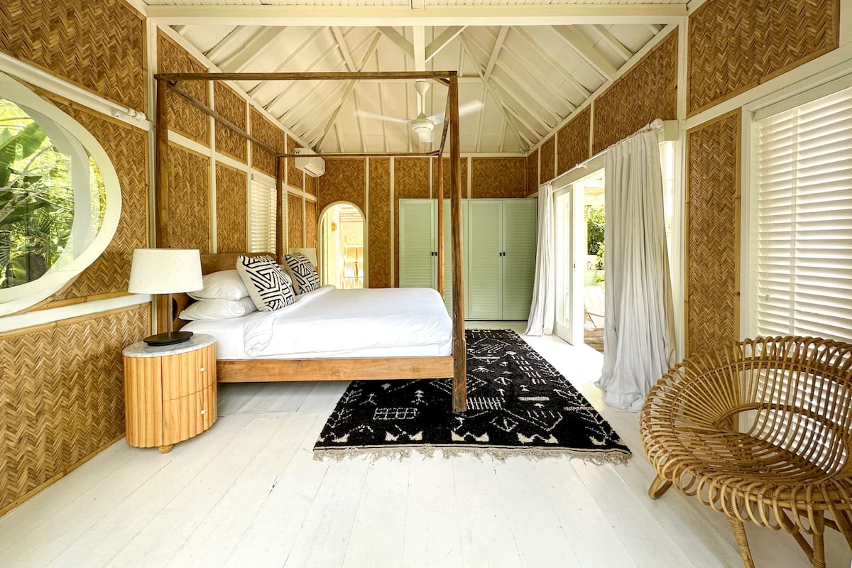 A spacious bedroom with a four-poster bed, a round window, and a view of the outdoors.