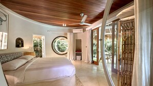 A bedroom with a bed, a ceiling fan, a window with a view of greenery, and a sliding glass door leading to an outdoor area. - Bodhi Bingin (Pecatu)