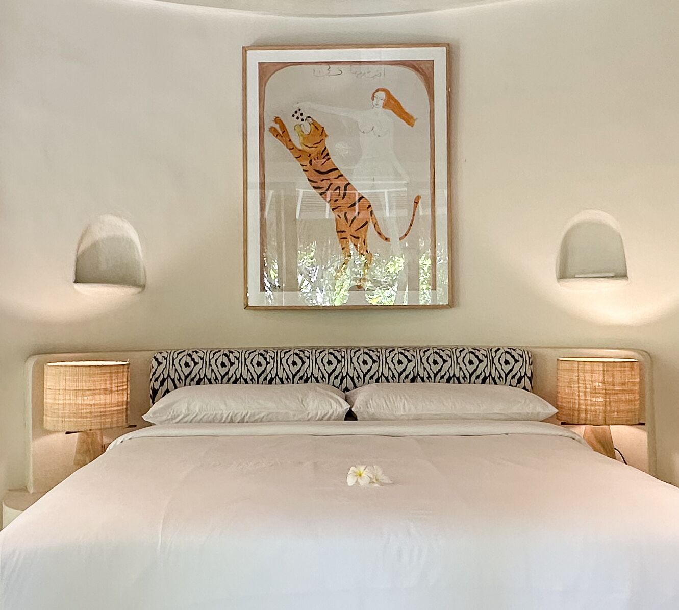 Un dormitorio con una cama, dos lámparas de noche, un cuadro enmarcado de un tigre y una flor sobre la cama.