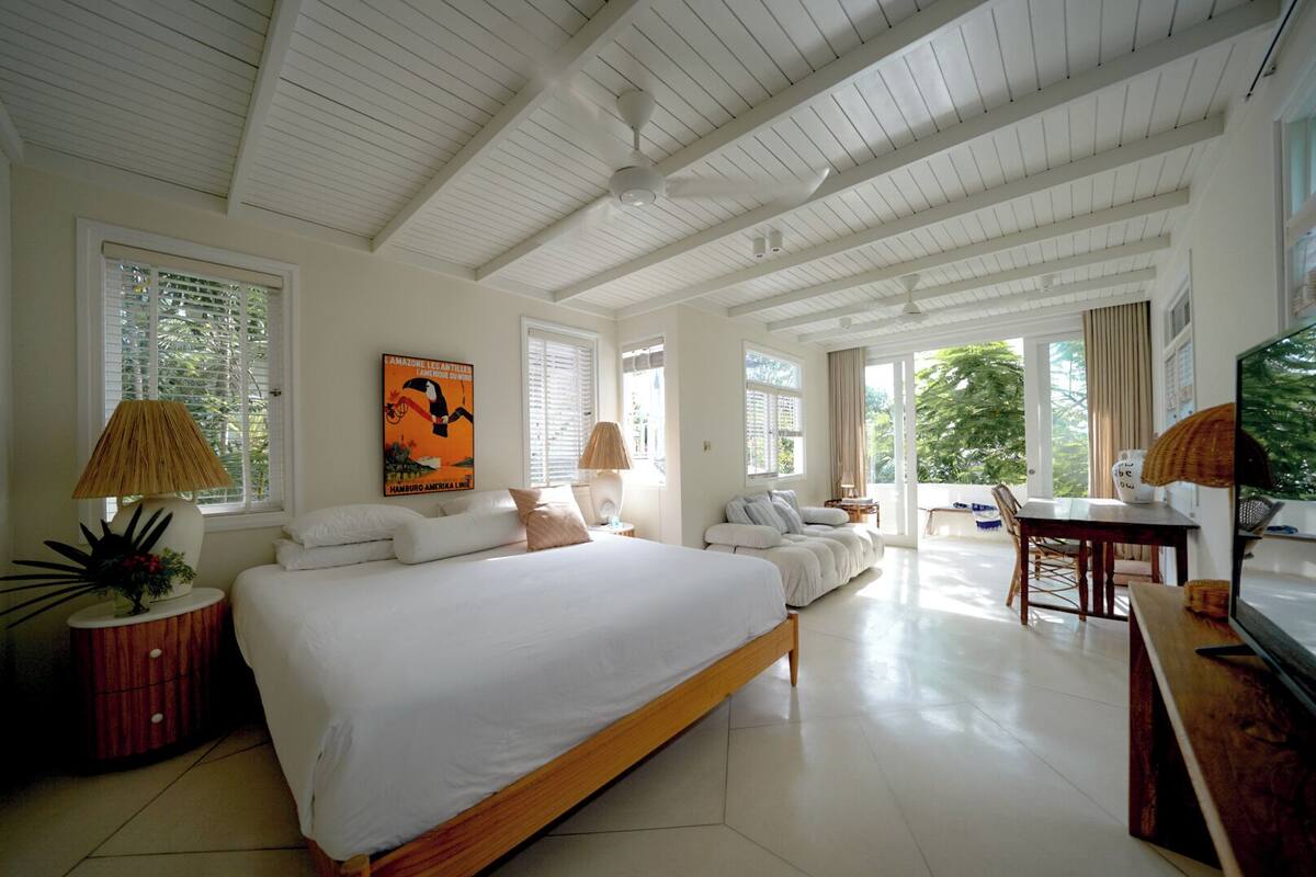 A spacious bedroom with a large bed, a sofa, a dining area, and a TV.