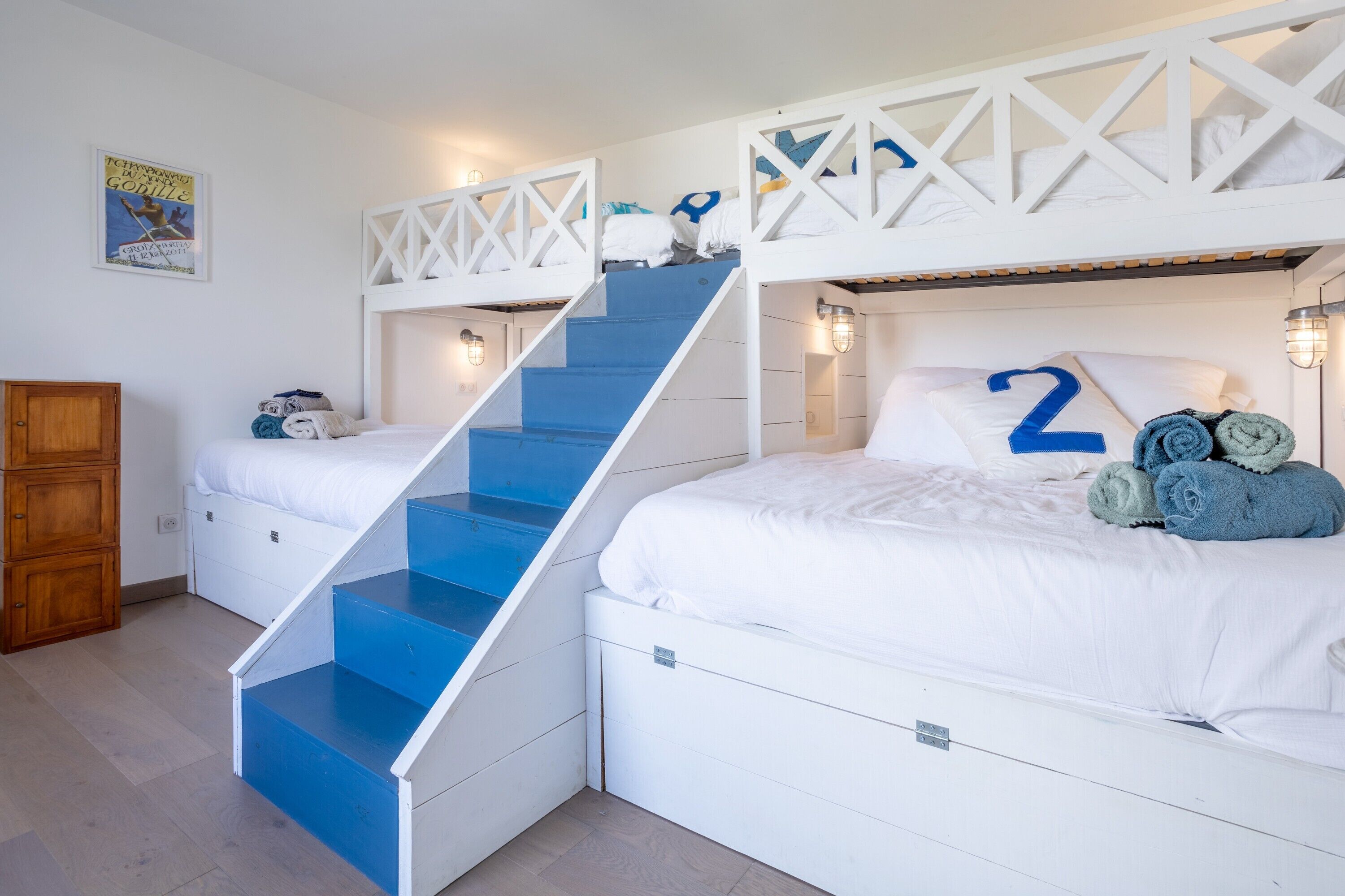 Une chambre avec des lits superposés, un escalier, une armoire en bois et une affiche accrochée au mur.