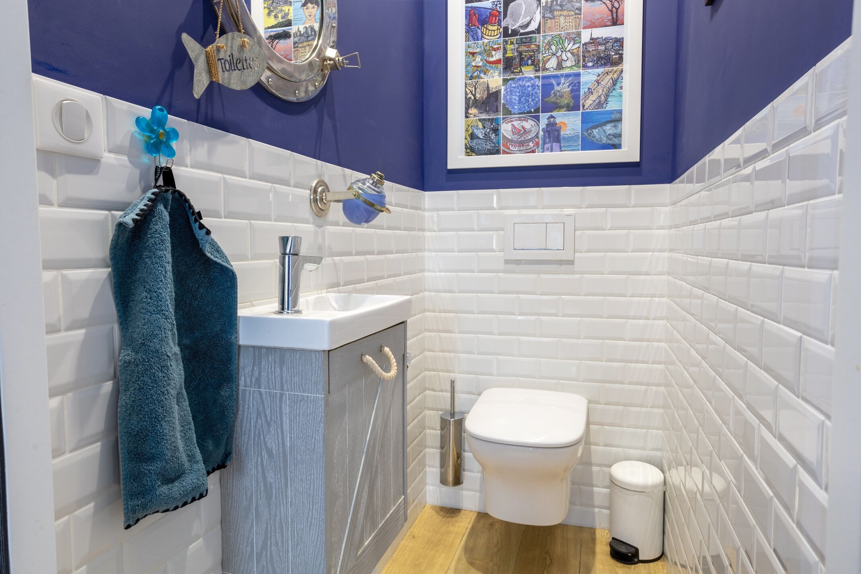 Een badkamer met een wit toilet, een wastafel met een blauwe handdoek en een decoratieve spiegel in de vorm van een vis.