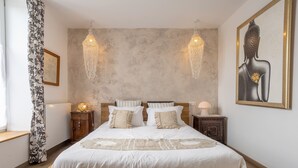Ein Schlafzimmer mit einem großen Bett, zwei Nachttischen, einer Pendelleuchte, einem gerahmten Kunstwerk und einem Fenster mit Vorhängen.