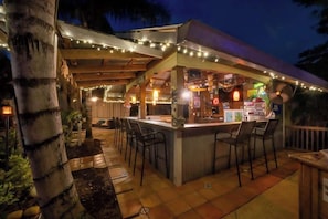 An outdoor bar area with a counter, bar stools, string lights, and a covered seating area.