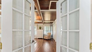 A hallway with wooden flooring, white doors with glass panels, and a ceiling with exposed beams.