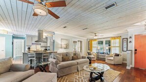 A spacious living area with a ceiling fan, a kitchen with white cabinets, and a dining area with yellow curtains.