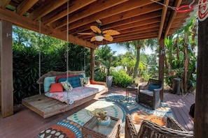 A covered outdoor seating area with a swing, wicker furniture, and a patterned floor.