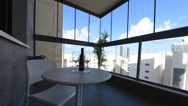 A balcony with a round table and two chairs, a potted plant, and a view of buildings and a crane. - The apartment in the hitech park Haifa (Haifa)
