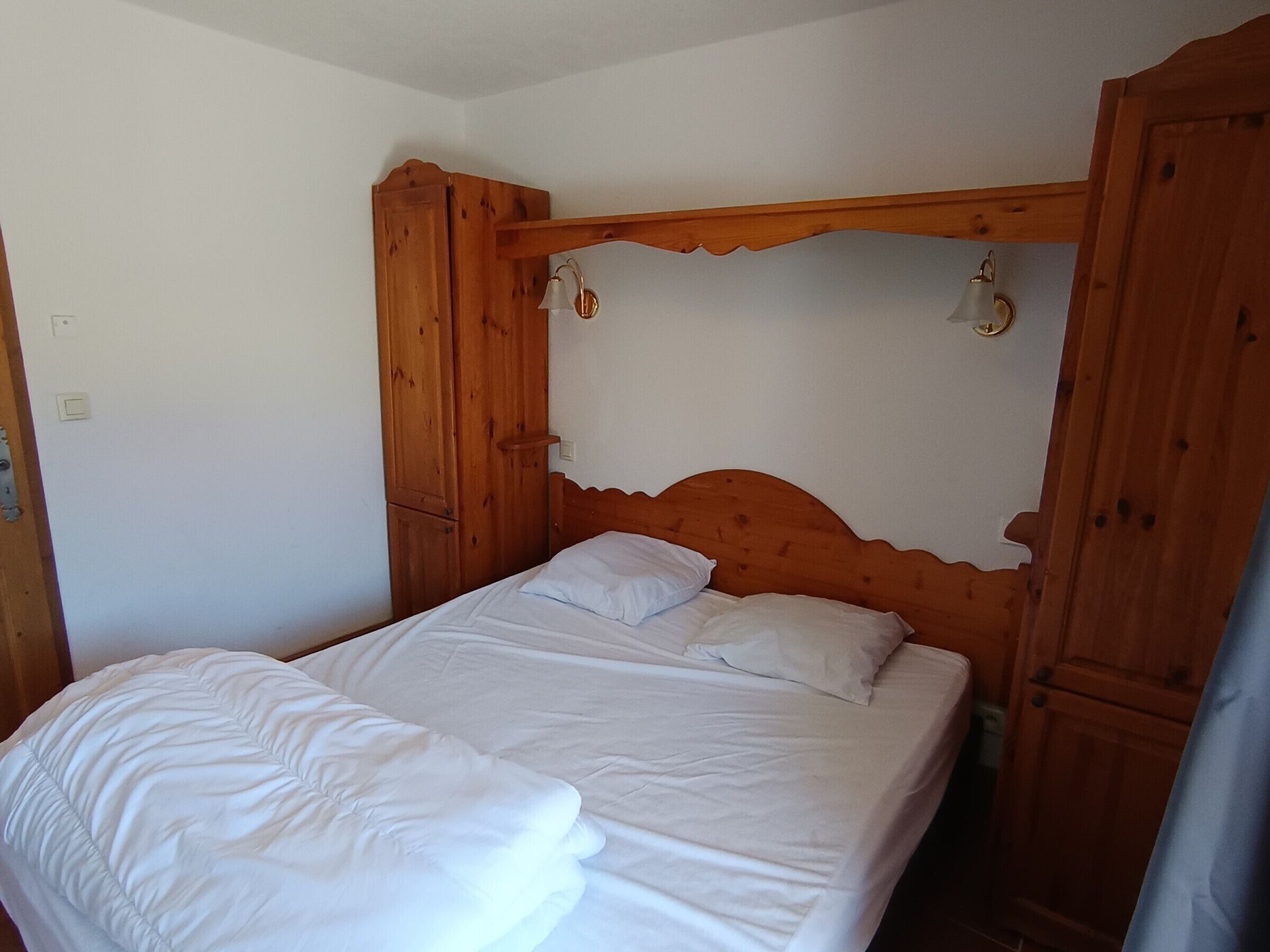 Ein hölzernes Bett mit weißer Bettwäsche in einem Zimmer mit weißen Wänden und Holzmöbeln.