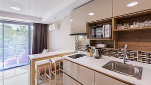 A modern kitchen with a central island, built-in microwave, and a large window with a view of greenery. - Rawai Beach Condo Room 407 (Rawai)