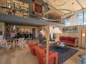 Un vaste espace de vie comprenant un piano, des étagères à livres, un canapé rouge et une table basse.
