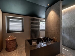 Sink area with wicker basket and large window with blinds.