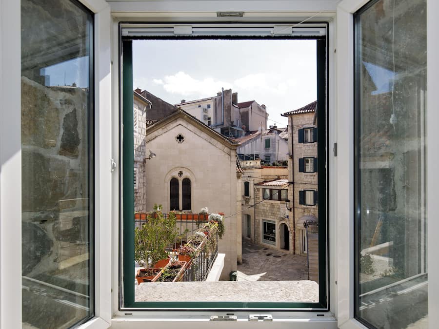 Vista desde una ventana a una calle estrecha con edificios históricos, incluyendo una iglesia con una cruz en la fachada.