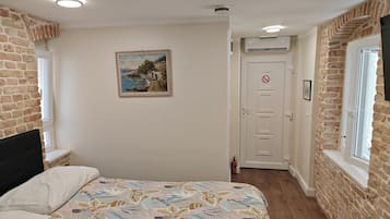 A bedroom with a bed, a painting, a door with a no-smoking sign, and brick walls.