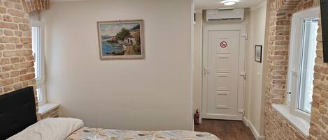 Quarto com uma cama, um quadro, uma porta com placa de proibido fumar e paredes de tijolo.