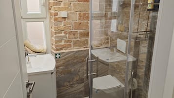 Uma casa de banho moderna com parede de pedra, cabine de duche em vidro e lavatório branco.