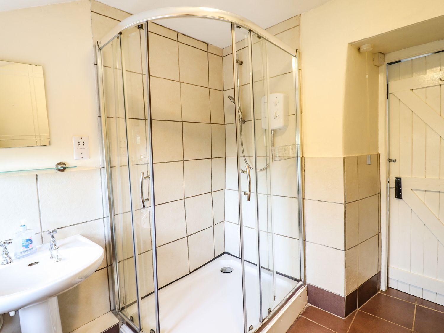 A bathroom with a glass shower enclosure, a white sink, and a tiled floor.