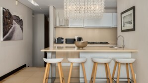 Een moderne keuken met een centraal eiland, barkrukken, een kroonluchter en een ingelijst schilderij aan de muur.