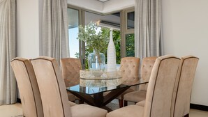 Een eettafel met zes beige stoelen met bekleding, een glazen blad en een witte vaas met groen.