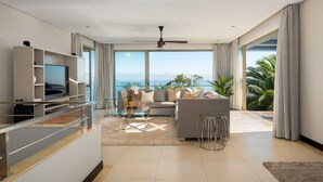 Een moderne woonkamer met een bank, televisie en een balkon met uitzicht op de oceaan.