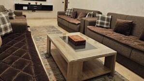 A modern living room with a sofa set, a coffee table, and a flat-screen TV mounted on the wall.