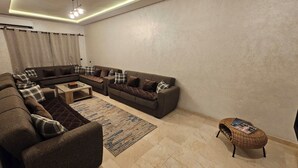 A living room with a sectional sofa, a coffee table, a rug, and a wicker ottoman.