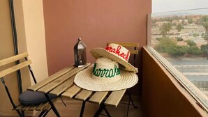 A balcony with a wooden table, two chairs, a straw hat, and a lantern.