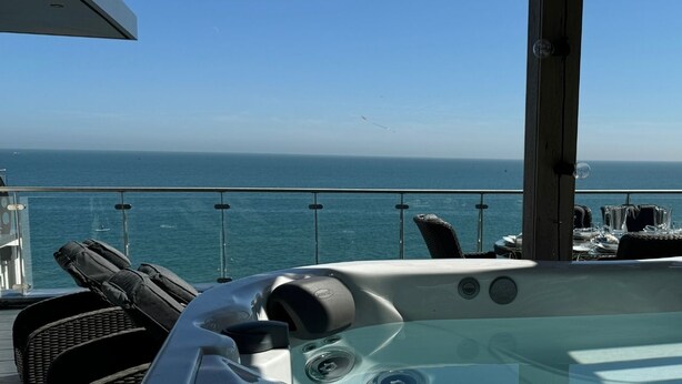 Un jacuzzi con vista al océano, sillas de descanso y una mesa de comedor en una terraza.