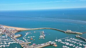 Vista aérea de un puerto deportivo costero con barcos amarrados, un muelle y una playa.