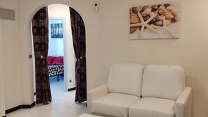 Ein Wohnzimmer mit einem weißen Sofa, einem weißen Couchtisch, einem Deckenventilator und einem Meeresmuschelbild an der Wand.