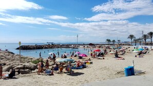 Ein Strand mit badenden Menschen, Sonnenschirmen und einer felsigen Küstenlinie.
