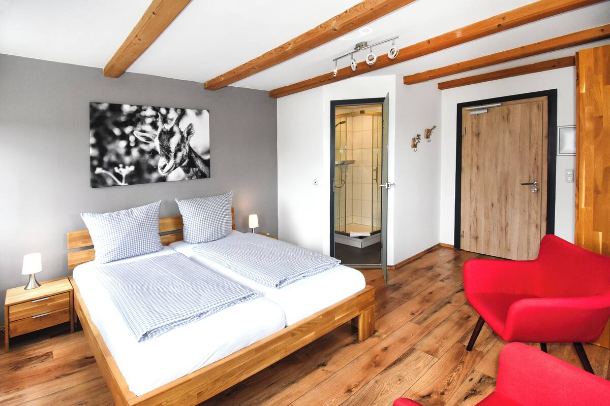 Ein Schlafzimmer mit einem hölzernen Bett, zwei Nachttischen, einem roten Sessel, einem Badezimmer mit Glastür und einem Holzschrank.
