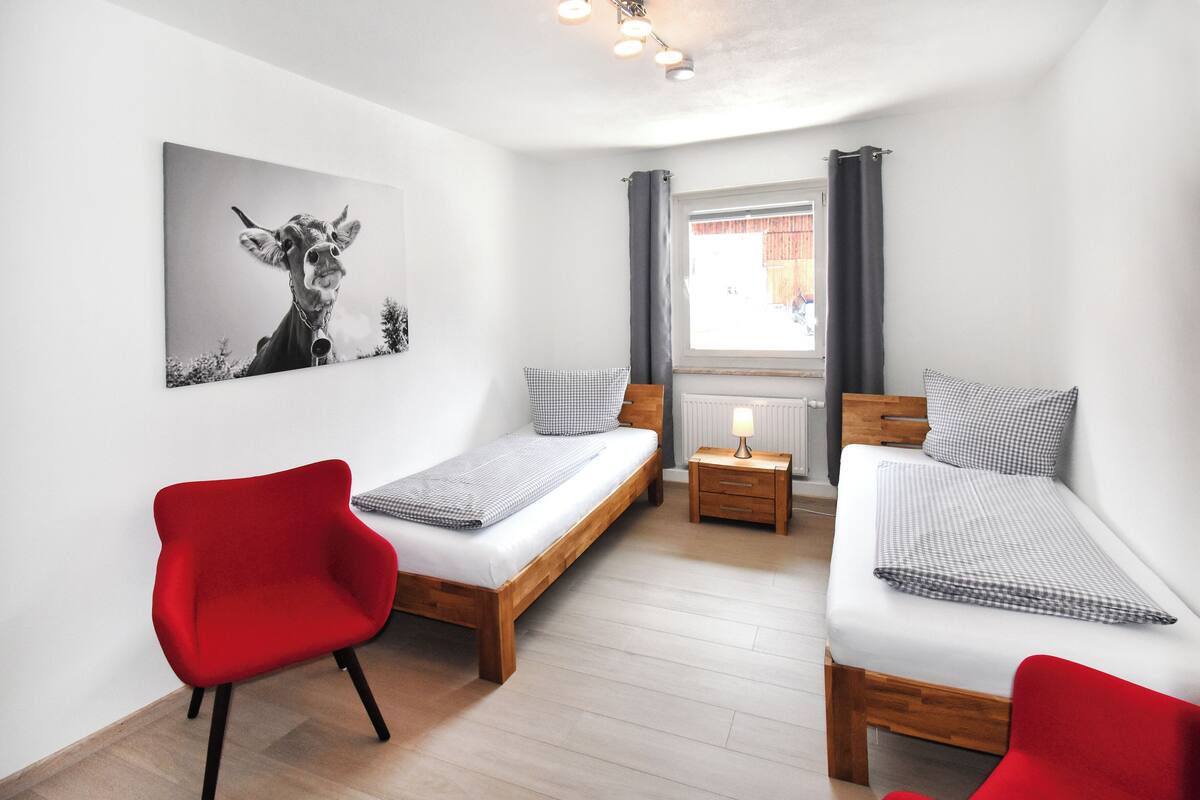 Ein Schlafzimmer mit zwei Einzelbetten, einem roten Sessel, einem kleinen Nachttisch mit Lampe und einem Wandbild mit Giraffe.