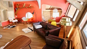 Un salon chaleureux avec un plafond en bois, un mur d’accent rouge, un canapé en cuir marron et une variété de fauteuils aux couleurs vives.