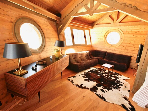 A cozy log cabin interior with a wooden desk, two lamps, a sofa, and a cowhide rug.