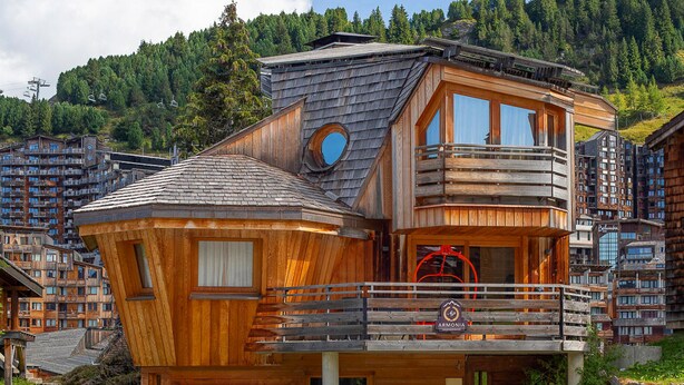Un chalet en bois doté d’un balcon, d’une fenêtre ronde et d’une enseigne portant l’inscription « ARMONIA ».