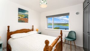 Een slaapkamer met een houten bed, uitzicht op de zee door een raam en een groene stoel.