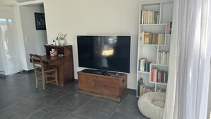 A living room with a flat-screen TV, a wooden coffee table, a bookshelf, and a white armchair. - Villa Avec Piscine Santa Maria Poggio (Santa-Maria-Poggio)