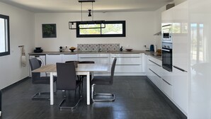 A modern kitchen with a dining area, featuring a built-in oven, a window with a view, and a dining table with chairs. - Villa Avec Piscine Santa Maria Poggio (Santa-Maria-Poggio)
