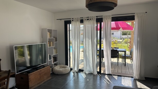 A modern living room with a flat-screen TV, a wooden cabinet, a grey sofa, and a dining area with a table and chairs. - Villa Avec Piscine Santa Maria Poggio (Santa-Maria-Poggio)