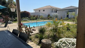 A pool area with a wooden deck, outdoor furniture, and a white building in the background. - Villa Avec Piscine Santa Maria Poggio (Santa-Maria-Poggio)