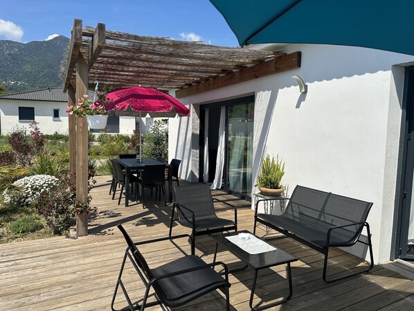 An outdoor patio with a wooden table and chairs, a red umbrella, and a potted plant.