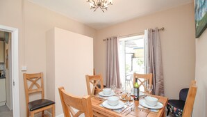 A dining area with a wooden table set for four, chairs, a chandelier, and a view of the outside. - The Skipper's House (Weymouth)