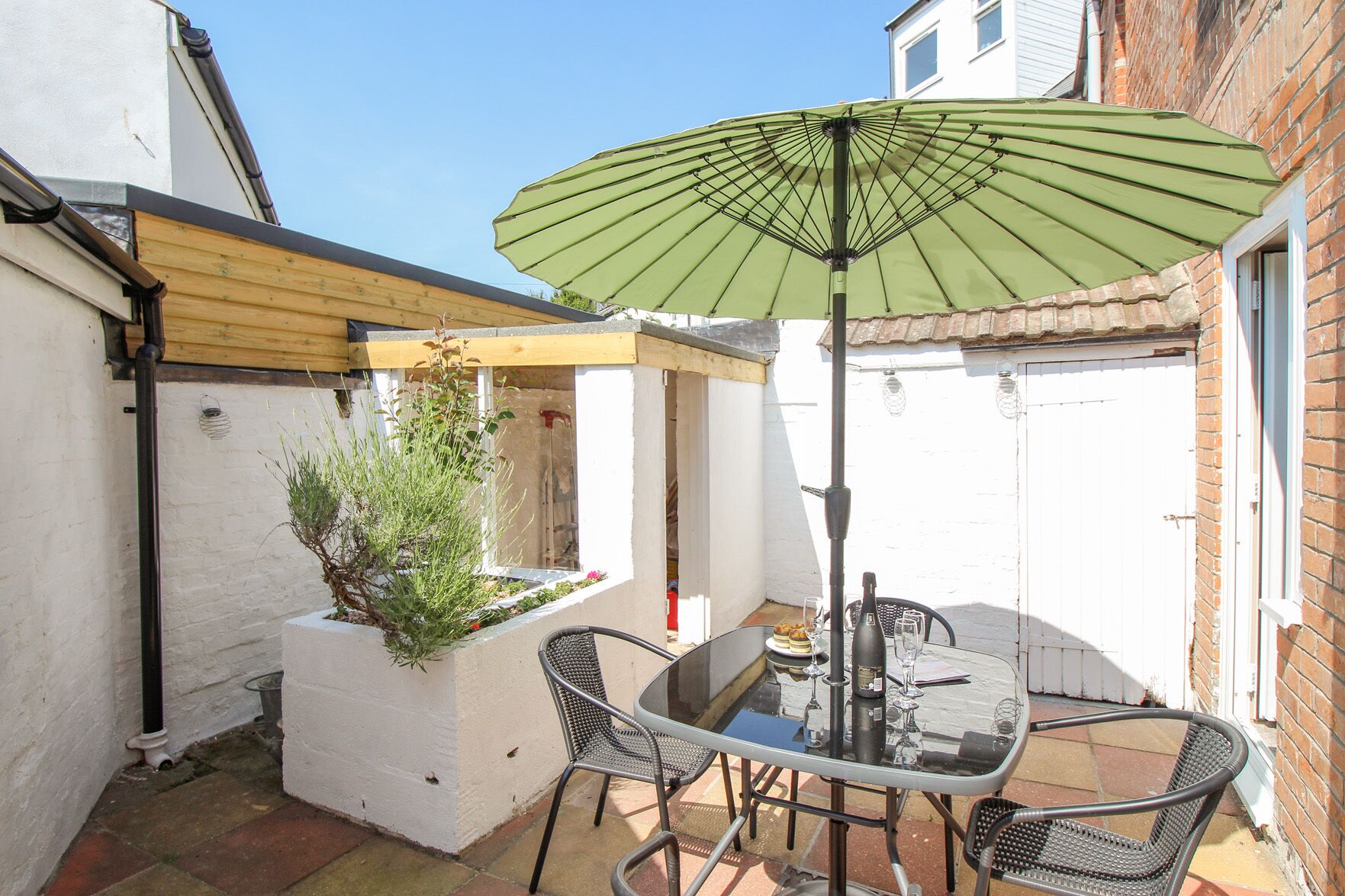 Une terrasse avec une table et des chaises, un parasol vert et une plante en pot.
