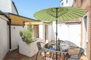 Un patio con una mesa, sillas, una sombrilla verde y una planta en maceta.