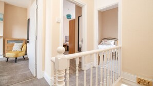 A staircase with a white railing leading to a bedroom with a bed and a nightstand. - The Skipper's House (Weymouth)